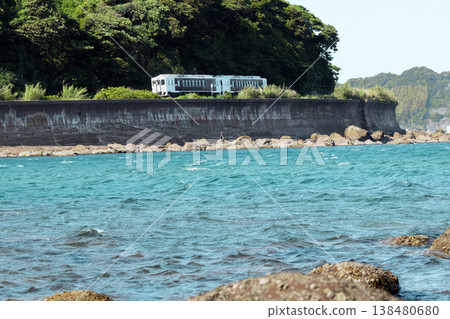 A JR Kyushu Nichinan Line Kiha 40 train runs across Sanno Beach in Nichinan City, Miyazaki Prefecture, under a clear blue sky. 138480680