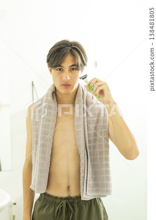Young teen boy with a towel over his shoulder and a shaving razor in bathroom. Young teen boy with a towel over his shoulder and a shaving razor in bathroom. 138481805