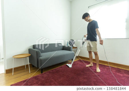 Young teen boy vacuuming floor with vacuum cleaner in living room. Young teen boy vacuuming floor with vacuum cleaner in living room. 138481844