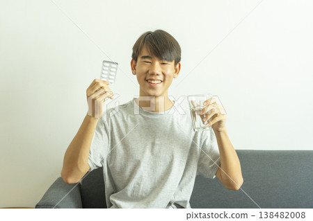 Teen boy holds a glass of water and pills. Takes medication for illness. Teen boy holds a glass of water and pills. Takes medication for illness. 138482008