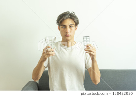 Teen boy holds a glass of water and pills. Takes medication for illness. 138482050