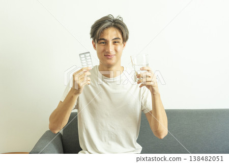 Teen boy holds a glass of water and pills. Takes medication for illness. 138482051