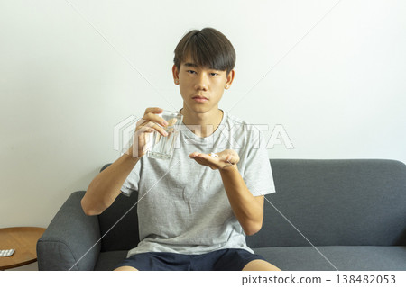 Teen boy holds a glass of water and pills. Takes medication for illness. Teen boy holds a glass of water and pills. Takes medication for illness. 138482053
