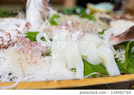A close-up of a boat-shaped platter of fresh squid and fish served at a banquet in a traditional Japanese inn. 138482784