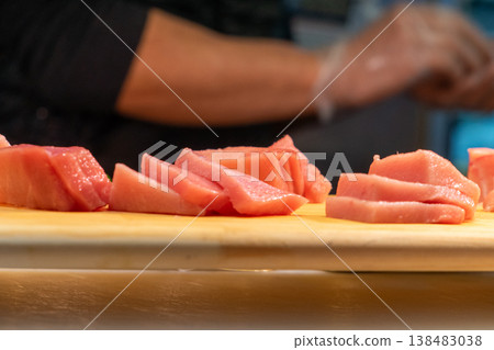 Fresh and tempting slices of tuna sashimi are arranged on a wooden cutting board at a Japanese kitchen counter. Fresh and tempting slices of tuna sashimi are arranged on a wooden cutting board at a Japanese kitchen counter. 138483038