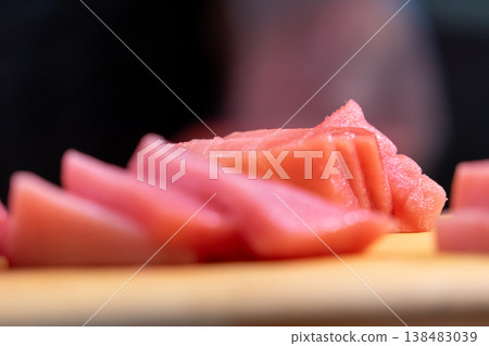 Fresh and tempting slices of tuna sashimi are arranged on a wooden cutting board at a Japanese kitchen counter. Fresh and tempting slices of tuna sashimi are arranged on a wooden cutting board at a Japanese kitchen counter. 138483039
