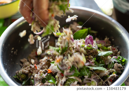 spicy mackerel salad with fresh herbs onion chili and lime being tossed by hand in metal bowl thai traditional dish bold flavor fresh ingredients and vibrant texture 138483179