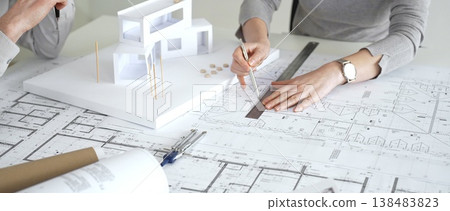 Architects discussing modern building design with 3d model and blueprints during planning meeting focused on innovation, teamwork and sustainable construction solutions, close up Architects discussing modern building design with 3d model and blueprints during planning meeting focused on innovation, teamwork and sustainable construction solutions, close up 138483823
