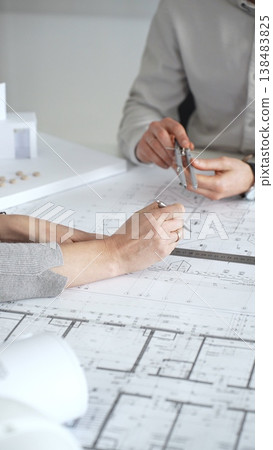 Architects discussing new construction project plans, working on blueprints with a contemporary house model, collaborating on urban design and future development, close up Architects discussing new construction project plans, working on blueprints with a contemporary house model, collaborating on urban design and future development, close up 138483825