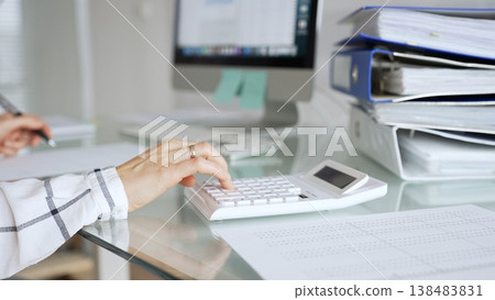 Woman calculating finances on a white calculator, managing budget and paperwork at office desk, preparing taxes. Audit and taxes in business Woman calculating finances on a white calculator, managing budget and paperwork at office desk, preparing taxes. Audit and taxes in business 138483831