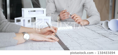 Architectural team analyzing building plans and a white scale model, discussing design concepts and construction details during a professional meeting in an office environment, close up Architectural team analyzing building plans and a white scale model, discussing design concepts and construction details during a professional meeting in an office environment, close up 138483894