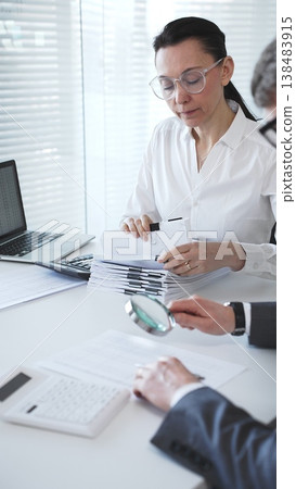 Professionals examining financial data and stacks of paperwork, performing a thorough audit and detailed investigation. Audit and taxes in business Professionals examining financial data and stacks of paperwork, performing a thorough audit and detailed investigation. Audit and taxes in business 138483915