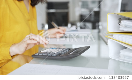 Woman in yellow blouse calculating finances, managing budget, doing taxes, working on accounting documents in office workspace. Audit and taxes in business Woman in yellow blouse calculating finances, managing budget, doing taxes, working on accounting documents in office workspace. Audit and taxes in business 138483937