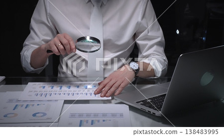 Businessman studying financial report data with magnifying glass, conducting detailed audit and analysis. Audit and taxes in business Businessman studying financial report data with magnifying glass, conducting detailed audit and analysis. Audit and taxes in business 138483995