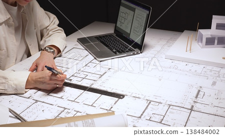 Architect working on detailed blueprints and precise floor plans, designing innovative construction projects, using a laptop and architectural model on a desk, close up Architect working on detailed blueprints and precise floor plans, designing innovative construction projects, using a laptop and architectural model on a desk, close up 138484002