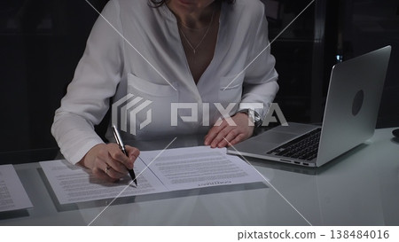 Businesswoman lawyer looking through a contract document before signing, while working in a corporate office at night. Audit, business and overworking concepts Businesswoman lawyer looking through a contract document before signing, while working in a corporate office at night. Audit, business and overworking concepts 138484016