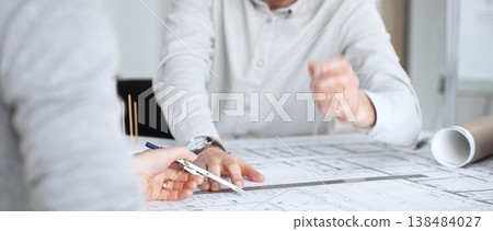 Architects collaborating over blueprints and a scaled model, discussing construction plans, urban development and design solutions in a modern office meeting setting, close up 138484027