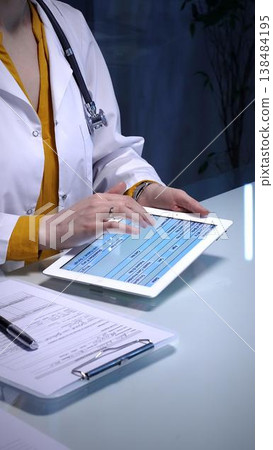 Doctor using digital tablet for remote patient data during an online consultation, managing electronic health records and telehealth services in a modern clinic Doctor using digital tablet for remote patient data during an online consultation, managing electronic health records and telehealth services in a modern clinic 138484195