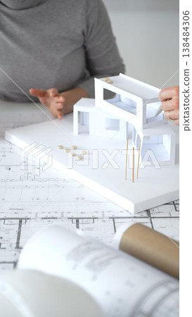 Architects discussing modern building design with 3d model and blueprints during planning meeting focused on innovation, teamwork and sustainable construction solutions, close up Architects discussing modern building design with 3d model and blueprints during planning meeting focused on innovation, teamwork and sustainable construction solutions, close up 138484306