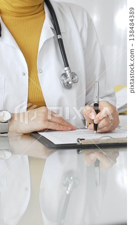 Female physician filling out medical documentation, preparing a diagnosis, or providing healthcare services in a clean, modern clinic. Concept of medicine, healthcare, and science Female physician filling out medical documentation, preparing a diagnosis, or providing healthcare services in a clean, modern clinic. Concept of medicine, healthcare, and science 138484389