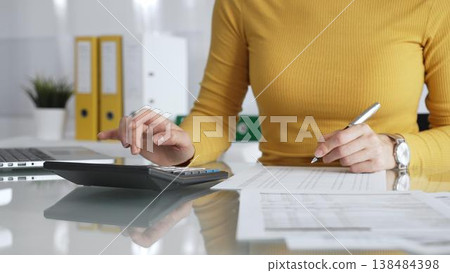 Woman working on financial documents, calculating budget using calculator and laptop, managing personal finances. Audit and taxes in business Woman working on financial documents, calculating budget using calculator and laptop, managing personal finances. Audit and taxes in business 138484398