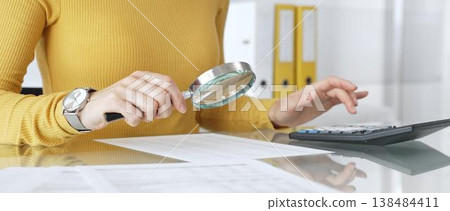 Woman doing financial paperwork, calculating budget, scrutinizing documents, and reviewing expenses with magnifying glass. Audit and taxes in business Woman doing financial paperwork, calculating budget, scrutinizing documents, and reviewing expenses with magnifying glass. Audit and taxes in business 138484411