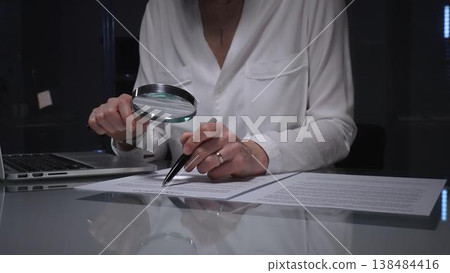 Businesswoman analyzing contract text with magnifying glass, scrutinizing fine print for legal details and agreement review. Audit, business concepts 138484416