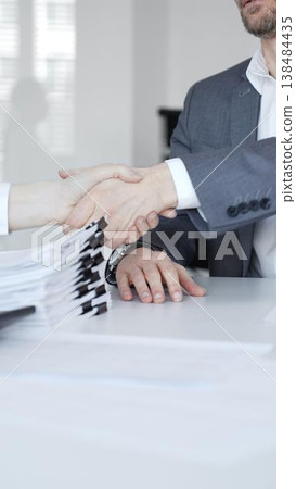 Business people shaking hands, concluding a partnership agreement after discussing documents and results. Audit and taxes in business 138484435