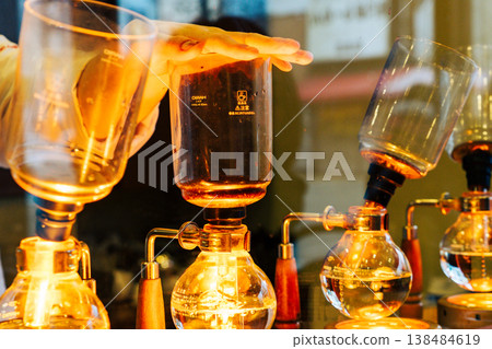 A close-up of the elegant process of a professional brewing coffee using a siphon coffee maker in a specialty coffee shop. A close-up of the elegant process of a professional brewing coffee using a siphon coffee maker in a specialty coffee shop. 138484619
