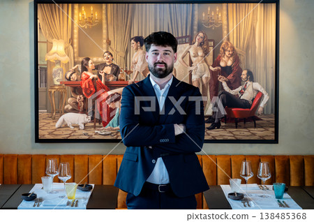 Male waiter in suit standing with arms crossed, confident restaurateur presence in front of large painting, management posture Male waiter in suit standing with arms crossed, confident restaurateur presence in front of large painting, management posture 138485368