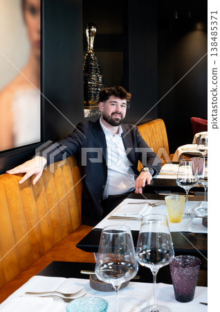 Male waiter in suit examining wine glass, sommelier vibe with focused tasting posture, curated beverage selection and intimate restaurant Male waiter in suit examining wine glass, sommelier vibe with focused tasting posture, curated beverage selection and intimate restaurant 138485371