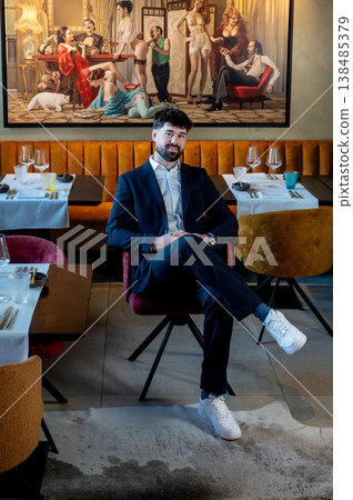 Male waiter in suit seated with leg crossed, relaxed executive dining scene with modern artwork and casual confidence during downtime Male waiter in suit seated with leg crossed, relaxed executive dining scene with modern artwork and casual confidence during downtime 138485379