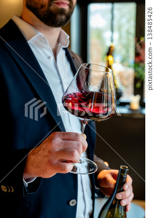 Sommelier navy suit holding wine glass, presenting bottle with confident posture and polished service in upscale modern restaurant. Warm Sommelier navy suit holding wine glass, presenting bottle with confident posture and polished service in upscale modern restaurant. Warm 138485426