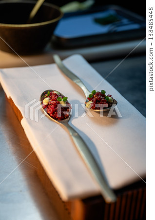 Two spoons with tartare on linen, blurred kitchen pass, shallow depth, chef plating motion, contemporary 138485448