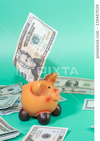 A piggy bank being filled with US currency, symbolizing savings or economic investment, with a backdrop of cash scattered around. 138487039