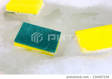 A dishwashing sponge floats in the foamy water of a dishwashing solution. A dishwashing sponge floats in the foamy water of a dishwashing solution. 138487294