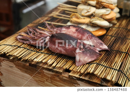 Whole squids on skewers ready to be grilled at a traditional Japanese street food stall. Whole squids on skewers ready to be grilled at a traditional Japanese street food stall. 138487488