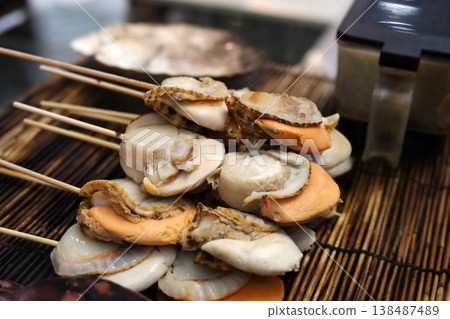 Large grilled scallops on skewers being prepared at a Japanese market. Large grilled scallops on skewers being prepared at a Japanese market. 138487489