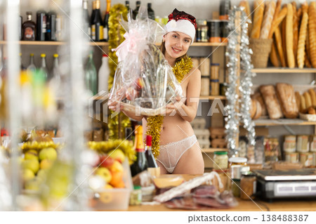 Happy topless girl in Santa hat with gift in hands celebrates Christmas in shop Happy topless girl in Santa hat with gift in hands celebrates Christmas in shop 138488387