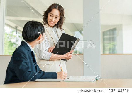 A female student in a school uniform studying at a cram school or preparatory school, and a female instructor teaching her. A female student in a school uniform studying at a cram school or preparatory school, and a female instructor teaching her. 138488726