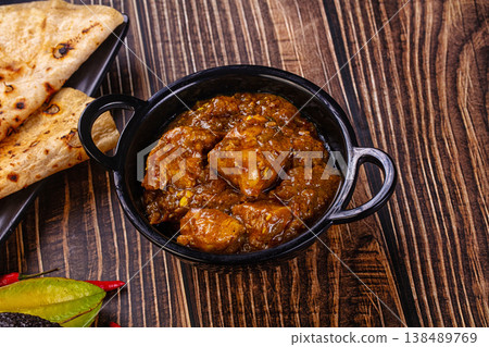 Bowl of traditional spicy chicken curma with flatbread, chilies, and exotic vegetables on a rustic dark wood table. Bowl of traditional spicy chicken curma with flatbread, chilies, and exotic vegetables on a rustic dark wood table. 138489769