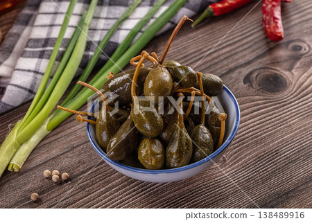 Pickled caper berries in a bowl with fresh ingredients on a rustic wooden table. Pickled caper berries in a bowl with fresh ingredients on a rustic wooden table. 138489916