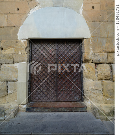 Ornate iron double door in weathered stone wall with arched lintel 138491751