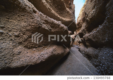 Narrow Pathway Through Rugged Slot Canyon Walls with Dramatic Natural Light 138493788