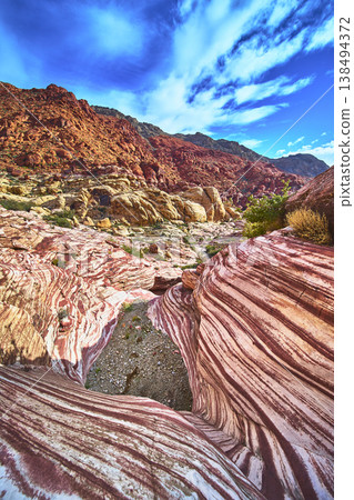 Striped Sandstone Formations and Red Cliffs Under Vibrant Sky in Nevada Desert 138494372