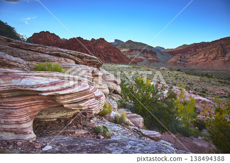 Red Rock Canyon Layered Sandstone Formations with Desert Vegetation and Distant Peaks 138494388