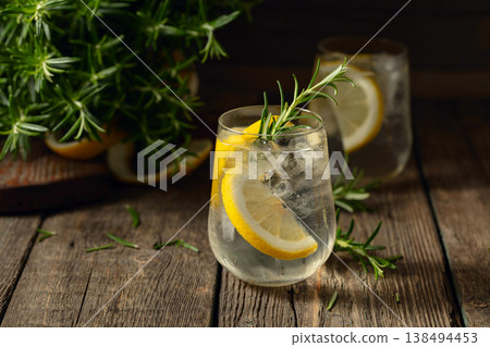 Cocktail gin tonic with ice, lemon, and rosemary on a old wooden table. Cocktail gin tonic with ice, lemon, and rosemary on a old wooden table. 138494453