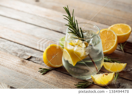Gin tonic with ice, rosemary, and lemon slices on an old wooden table. Gin tonic with ice, rosemary, and lemon slices on an old wooden table. 138494478