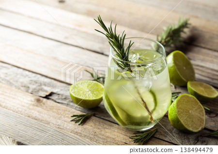 Gin tonic with ice, rosemary, and lime slices on an old wooden table. 138494479
