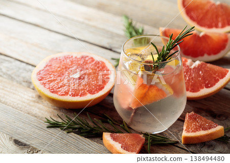 Gin tonic with ice, rosemary, and grapefruit slices on an old wooden table. 138494480